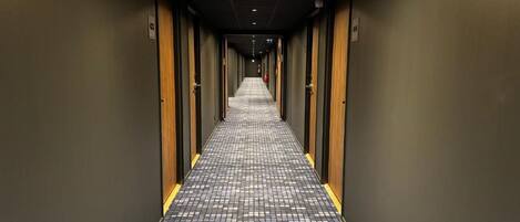 Un pasillo de hotel con suelo a cuadros, puertas a ambos lados y un extintor en la pared.