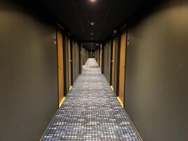 Un pasillo de hotel con suelo a cuadros, puertas a ambos lados y un extintor en la pared.