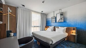 Moderni hotellihuone, jossa on suuri sänky, työpöytä, tuoli ja vaatekaappi.