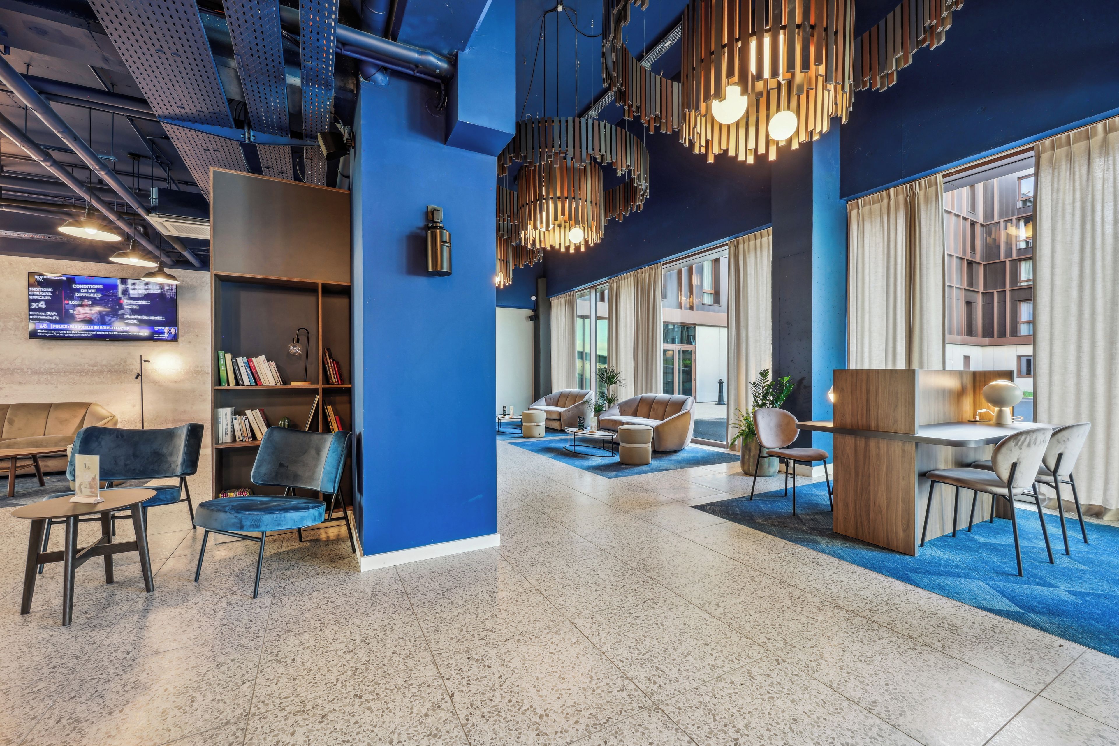 A modern lobby with a blue accent wall, a bookshelf, seating areas, and a large window providing natural light.