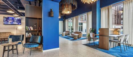 A modern lobby with a blue accent wall, a bookshelf, seating areas, and a large window providing natural light.