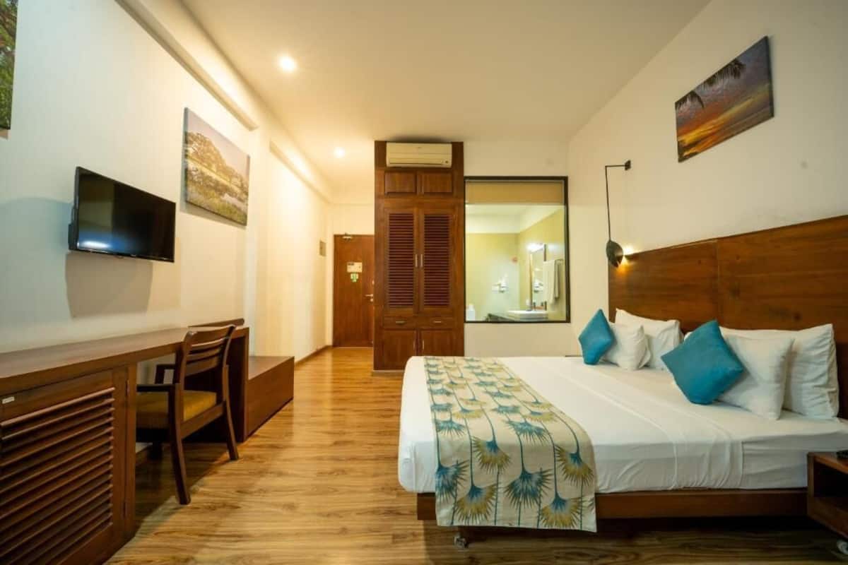 Un dormitorio con cama, mesita de noche, televisor y un escritorio de madera.