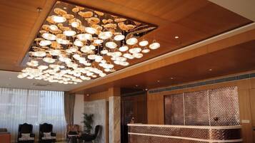 A hotel lobby with a large chandelier, seating area with chairs, and a reception desk.
