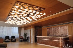 A hotel lobby with a large chandelier, seating area, reception desk, and a patterned wall.