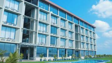 A multi-story hotel with balconies, a swimming pool, and a clear sky.