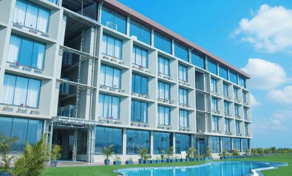 A multi-story hotel with balconies, a swimming pool, and a clear sky. - Soulbay By Jpw Resort (Garudeshwar)