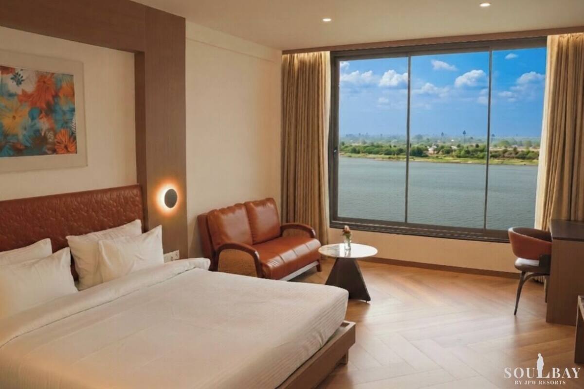 A hotel room with a bed, a sofa, a small table, and a view of a body of water.