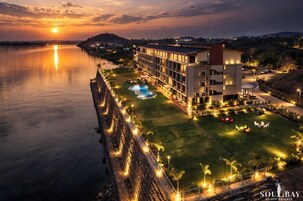 A hotel with a swimming pool, a well-lit lawn, and a view of the sunset over a body of water.