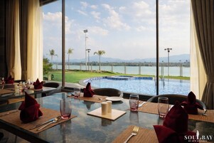 A dining area with tables set for two, overlooking a pool and a view of the water and distant landscape.