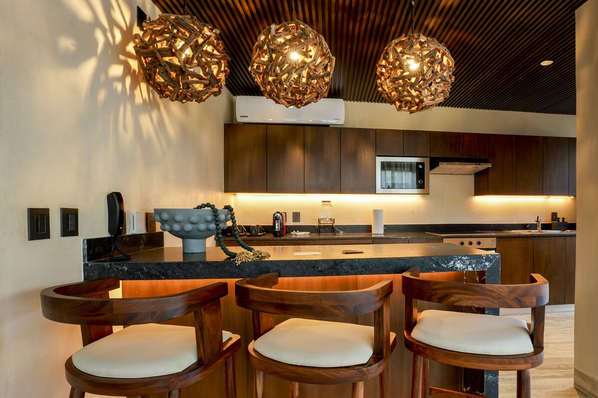 A modern kitchen with wooden bar stools, pendant lighting, and a central island.