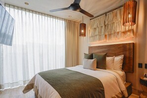 A hotel room with a large bed, a ceiling fan, a wooden headboard, and a large window with curtains. - Trobbu (Tulum)