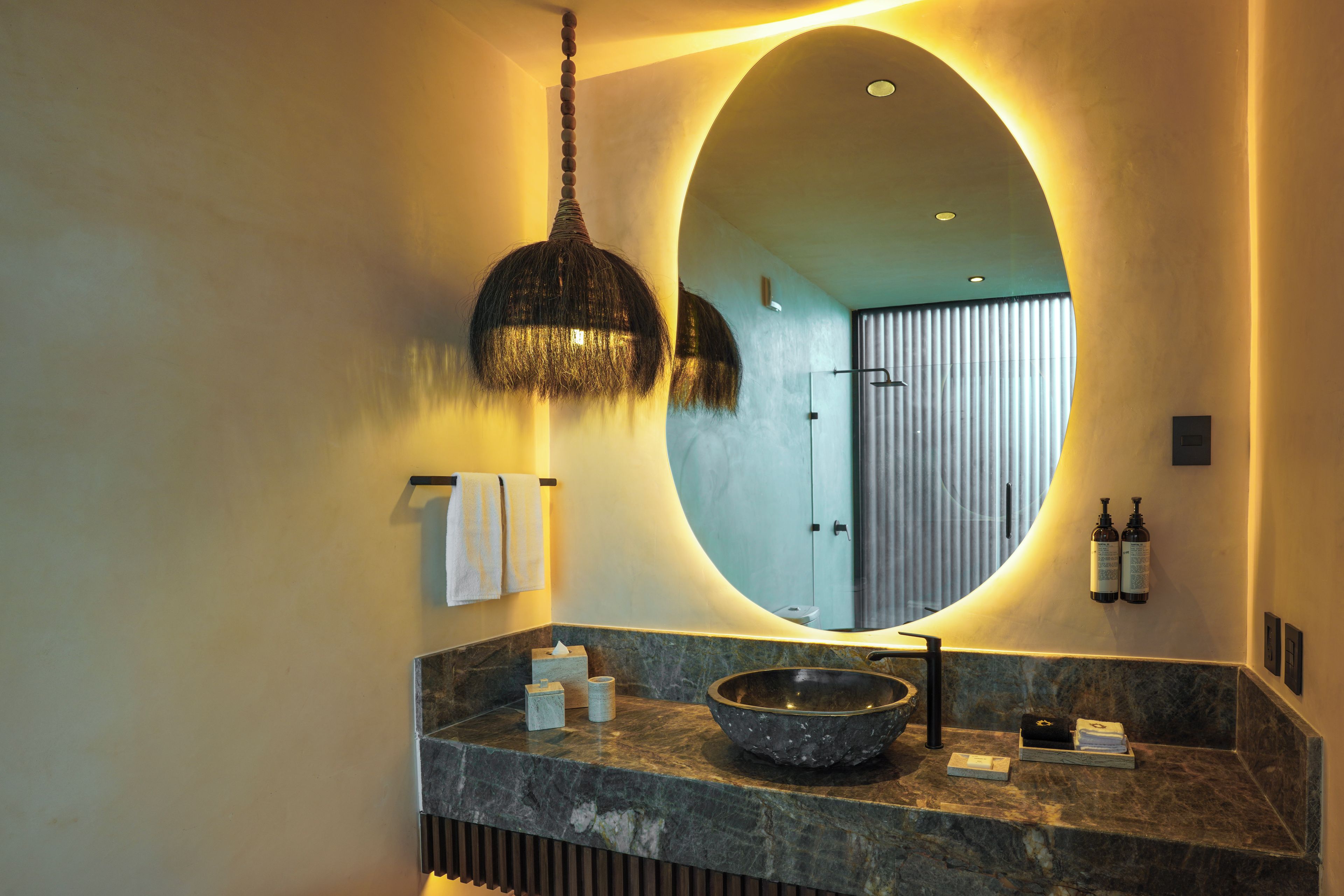 Une salle de bain dotée d’un grand miroir ovale, d’un lavabo en pierre et d’un luminaire suspendu.