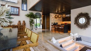 A spacious living area with a dining table, sofas, and a kitchen in the background. - Trobbu (Tulum)