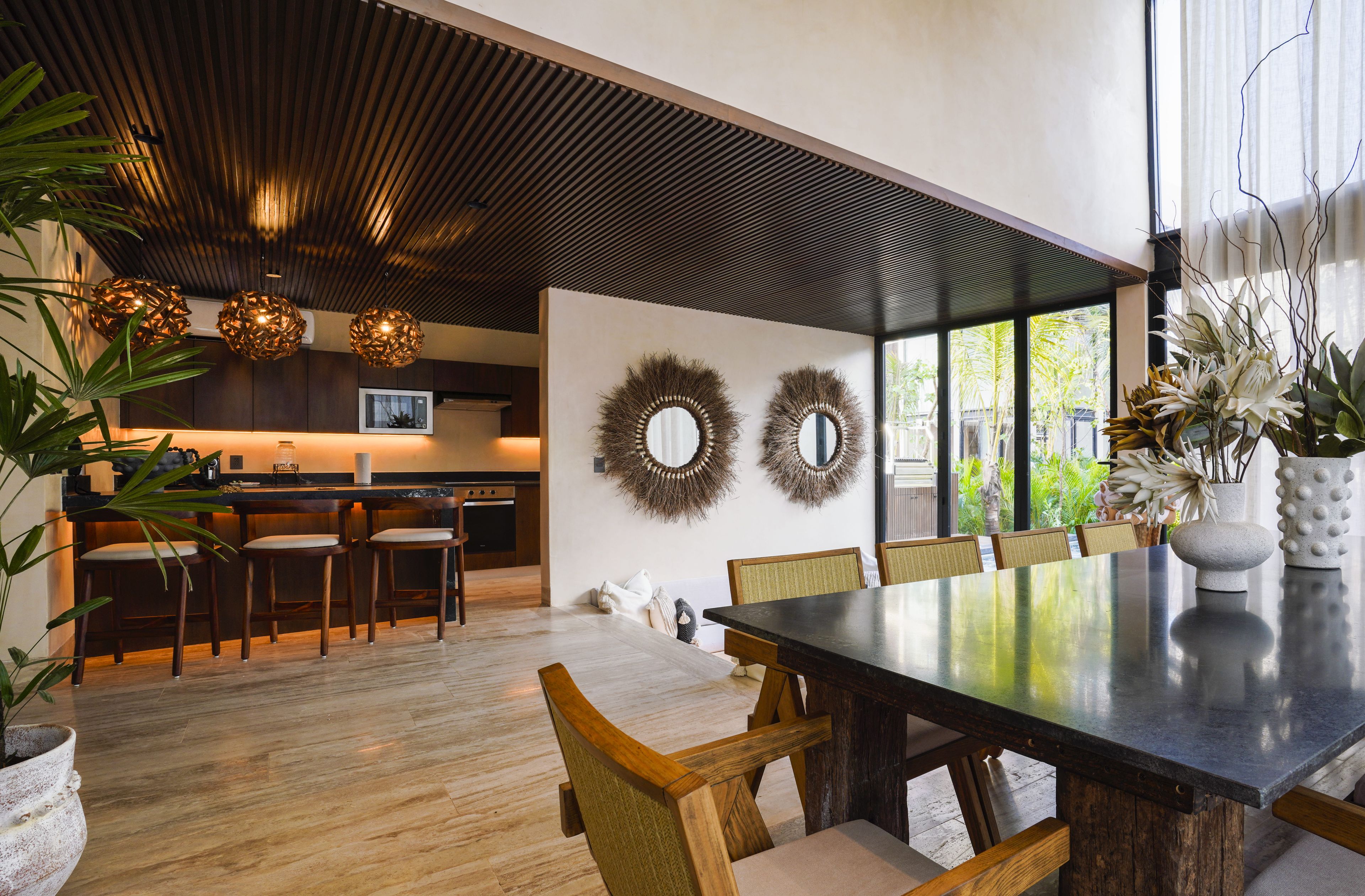 Un comedor moderno con una mesa grande, sillas de madera y una cocina al fondo.