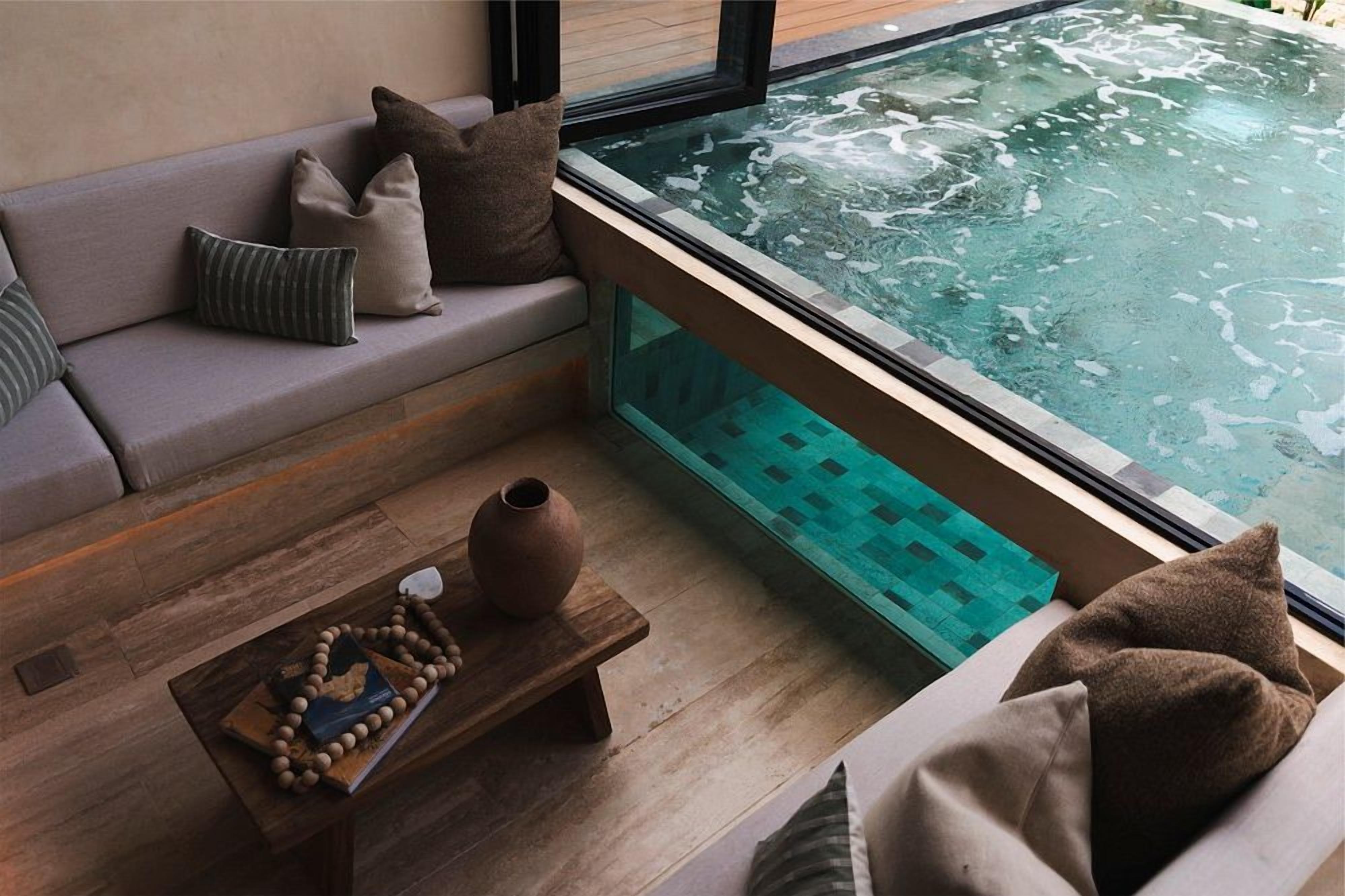 Un área de spa con un jacuzzi, un banco de madera con un jarrón y un libro, y un sofá con cojines.