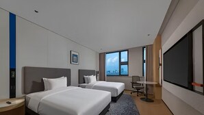 Quarto de hotel com duas camas, uma janela grande, televisão de tela plana e uma escrivaninha.