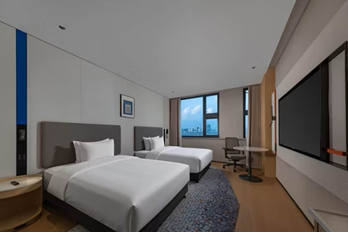 Ein Hotelzimmer mit zwei Betten, einem großen Fenster, einem Flachbildfernseher und einem Schreibtisch.