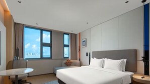 Quarto de hotel com cama, escrivaninha, cadeira e janela com vista para a cidade.