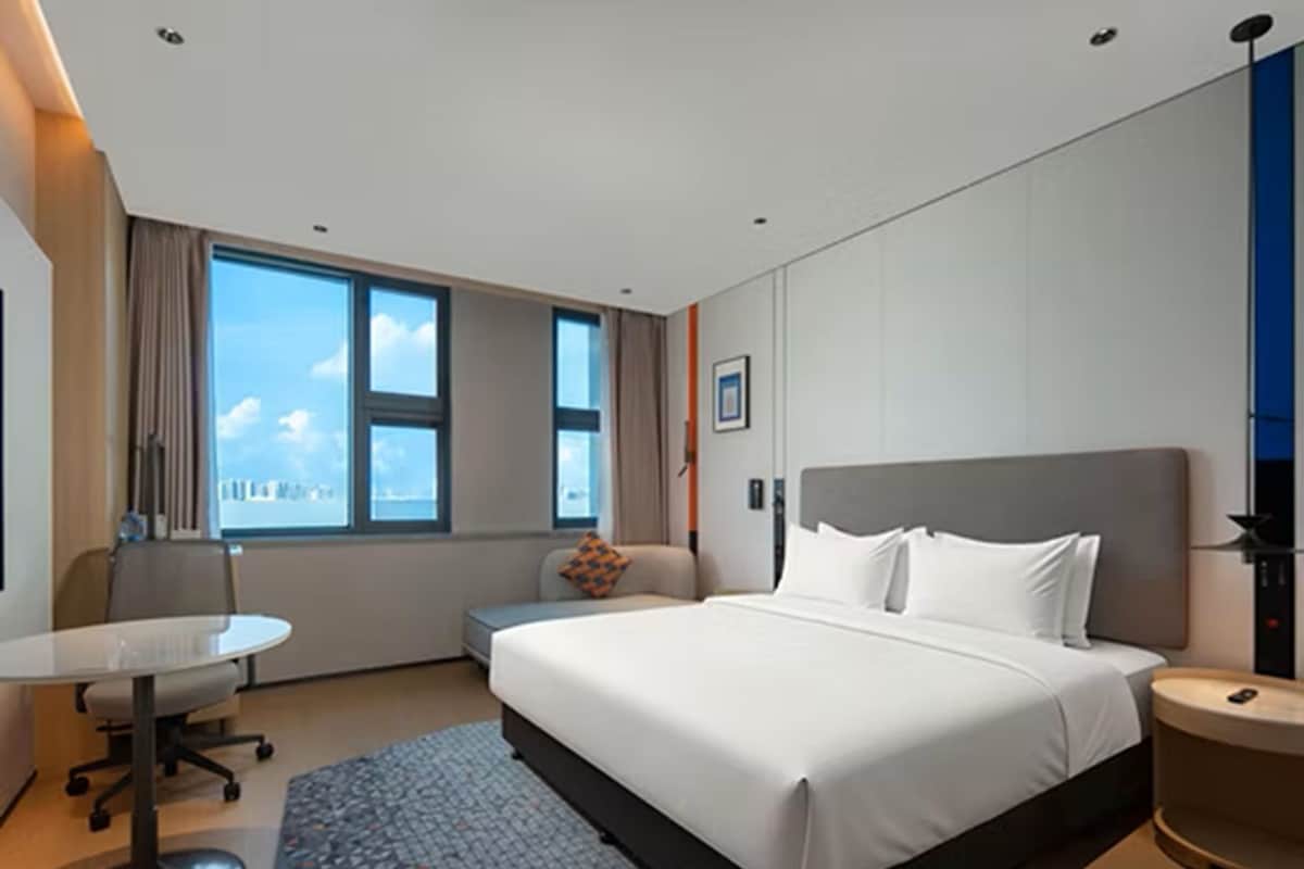 Ein Hotelzimmer mit Bett, Schreibtisch, Stuhl und Fenster mit Blick auf die Stadt.