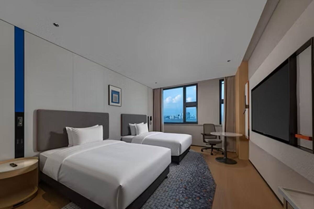 Habitación de hotel con dos camas, un ventanal grande, un televisor de pantalla plana y un escritorio.