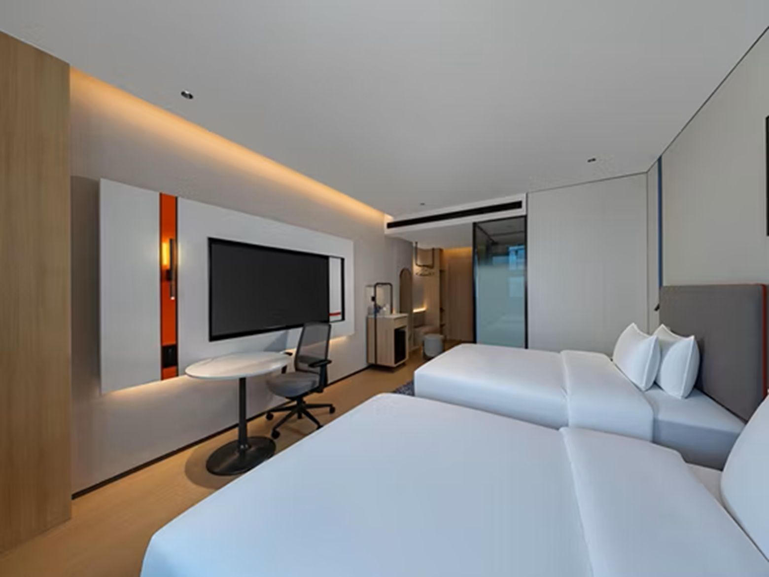 A modern hotel room with a large bed, a desk, and a flat-screen TV mounted on the wall.
