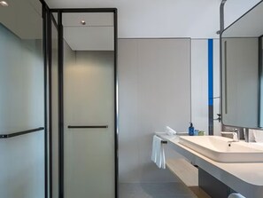 Een moderne badkamer met een douchecabine van glas, een grote spiegel en een wastafelmeubel met wastafel en handdoekhouder.