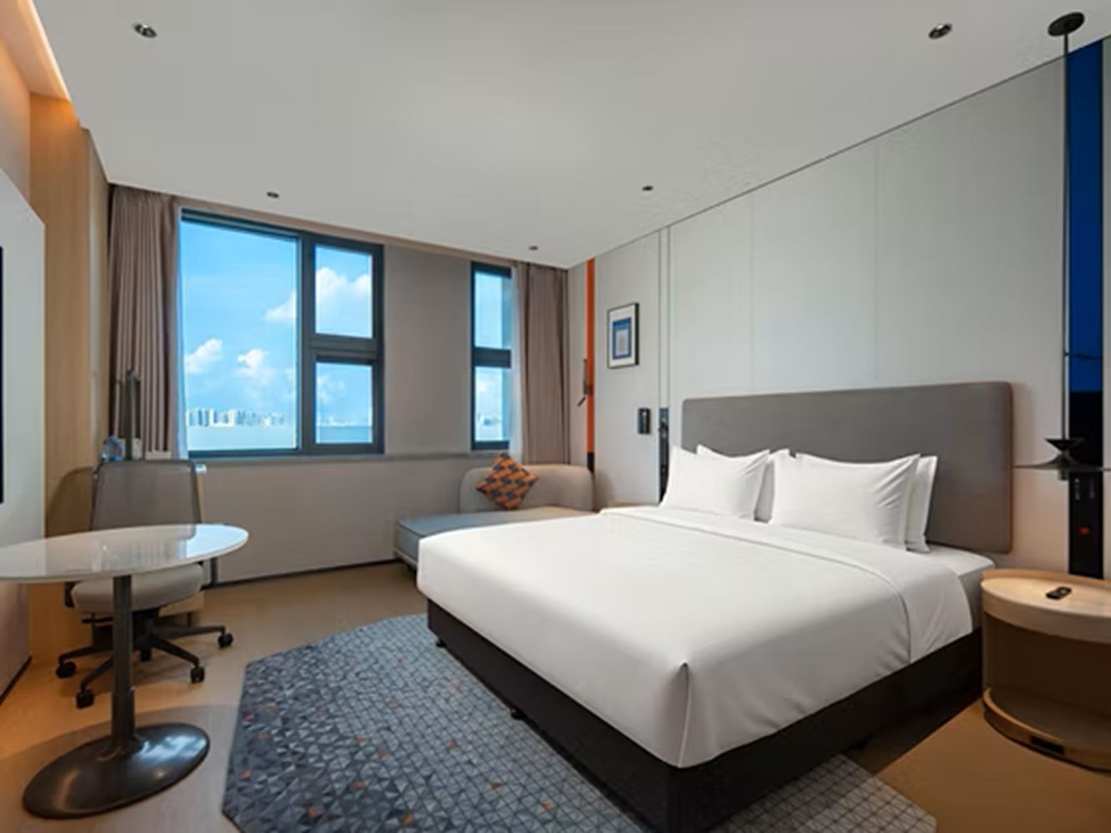 Quarto de hotel com cama, escrivaninha, cadeira e janela com vista para a cidade.