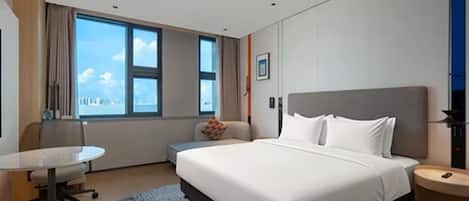 Quarto de hotel com cama, escrivaninha, cadeira e janela com vista para a cidade.