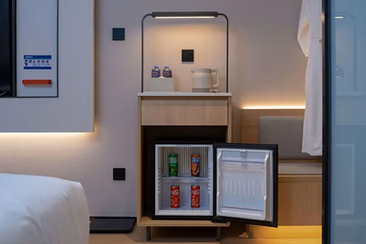 Una habitación de hotel compacta con una cama, una kitchenette pequeña con refrigerador, microondas y cafetera.
