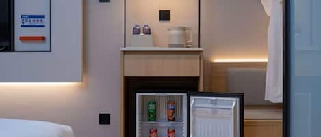 A compact hotel room with a bed, a small kitchenette with a refrigerator, a microwave, and a coffee maker.