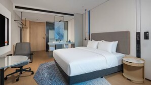 Quarto de hotel moderno com cama grande, escrivaninha e banheiro.
