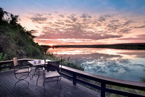Een houten terras met een tafel en stoelen met uitzicht op een kalm meer bij zonsondergang.