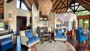 Une pièce spacieuse avec un plafond haut, un grand lustre, un lit à baldaquin et un coin repas avec des chaises bleues.