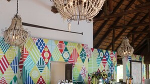 Un espace bar agrémenté d’un mur aux motifs géométriques colorés, de tabourets de bar en bois et d’un luminaire suspendu au plafond, dont l’abat-jour est fait de fibres tressées.