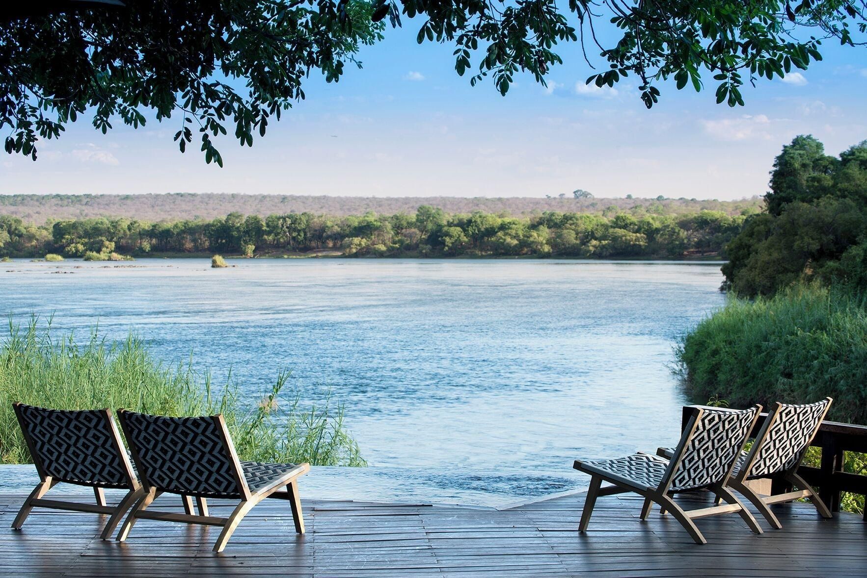 Una terraza con dos sillones de descanso frente a un río tranquilo, rodeada de follaje y árboles.