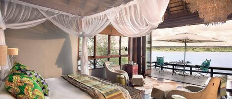 A room with a bed, a chair, a table, and a view of a body of water.