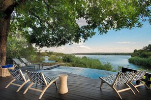 Een terras met loungebedden en een klein zwembad met uitzicht op een rivier.
