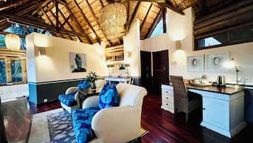 A spacious room with a high ceiling, a large chandelier, a sofa with blue cushions, a dining area with a white table, and artwork on the walls.
