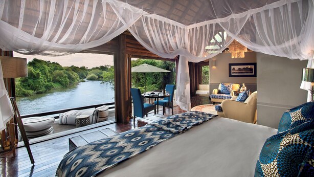 Une chambre avec un grand lit, un coin salon avec une table et des chaises, et une vue sur une rivière.