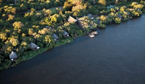 Vista aérea de un complejo turístico junto al lago, con varias cabañas de techo de paja conectadas por un estrecho sendero.