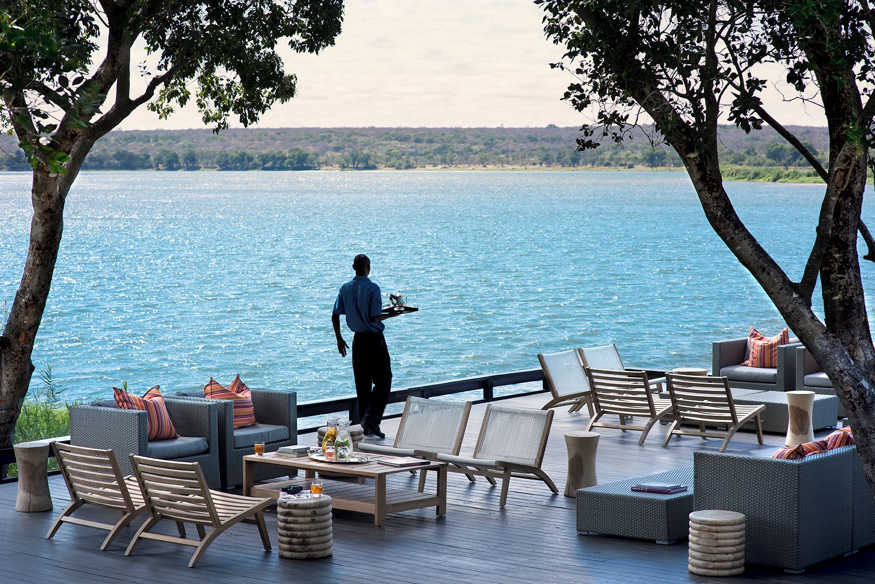 A deck with outdoor seating, a waiter, and a view of a large body of water.