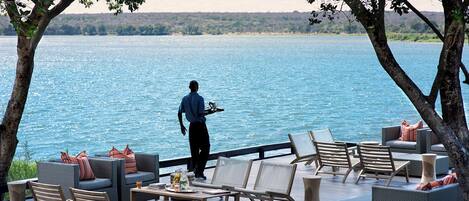 A deck with outdoor seating, a waiter, and a view of a large body of water.