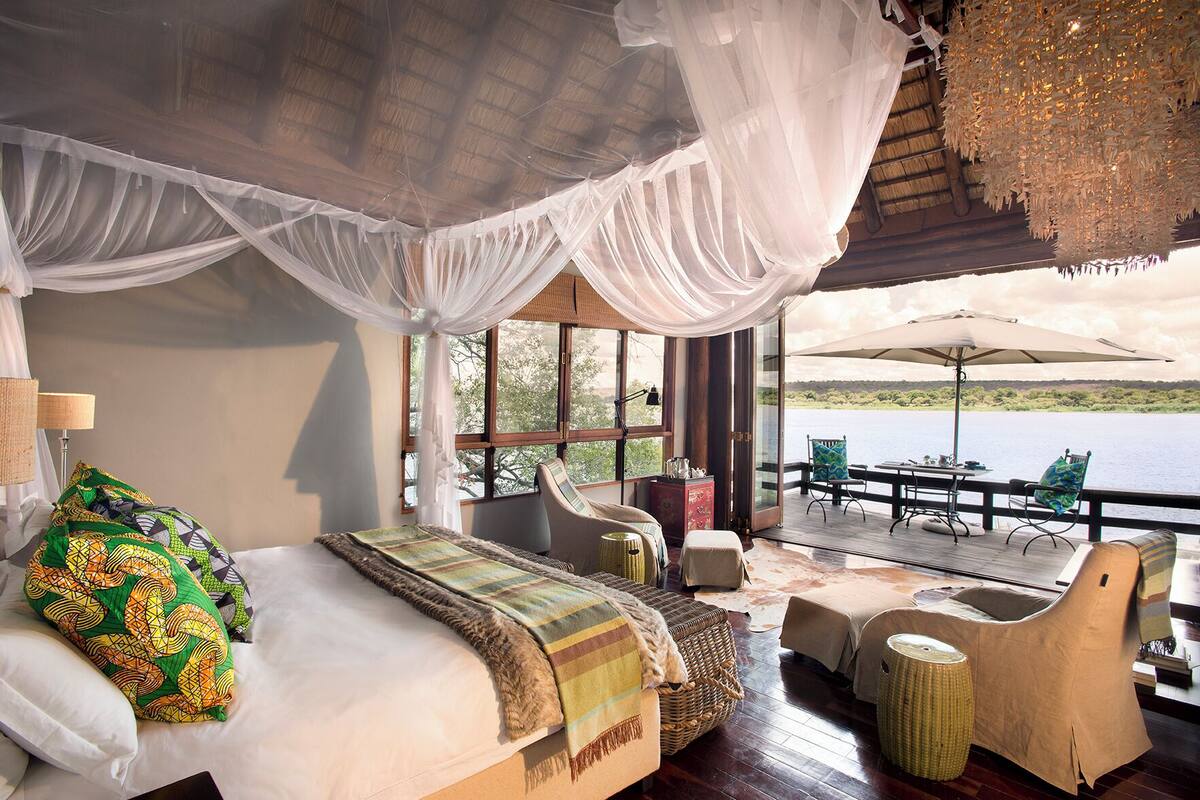 A room with a bed, a chair, a table, and a view of a body of water.