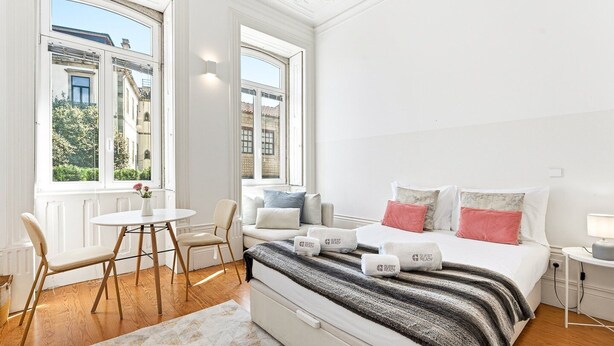 A modern hotel room with a bed, bedside table, and a view of the city. - GuestReady - studio in Santa Catarina (Porto)