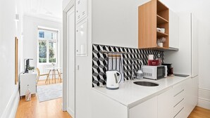 A modern kitchen with white cabinetry, a black and white patterned backsplash, and a wooden shelf above the countertop. - GuestReady - studio in Santa Catarina (Porto)
