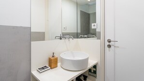 A bathroom with a white sink, a mirror, a towel dispenser, and a door. - GuestReady - studio in Santa Catarina (Porto)