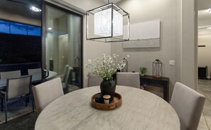 A modern dining area with a round table, chairs, a vase with flowers, a tray with items, a pendant light, and a glass partition. - Three bedroom  house with beautiful pool (Lake Havasu City)