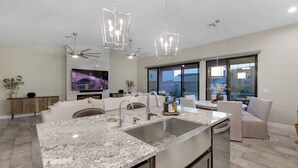 Une cuisine moderne dotée d’un grand îlot central, d’appareils électroménagers en acier inoxydable et de luminaires suspendus.