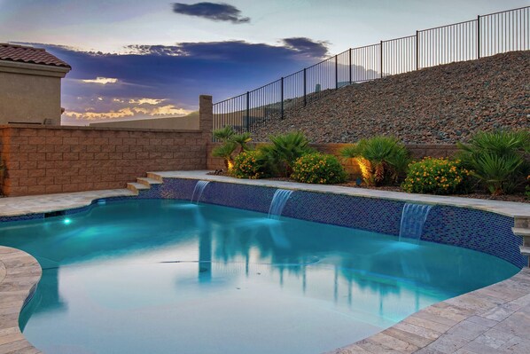A swimming pool with a waterfall feature, surrounded by a stone wall and a metal fence. - Three bedroom  house with beautiful pool (Lake Havasu City)