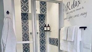 Een badkamer met een glazen douchecabine, betegelde vloer, een witte handdoekhouder en een bordje met de tekst 'Relax'.